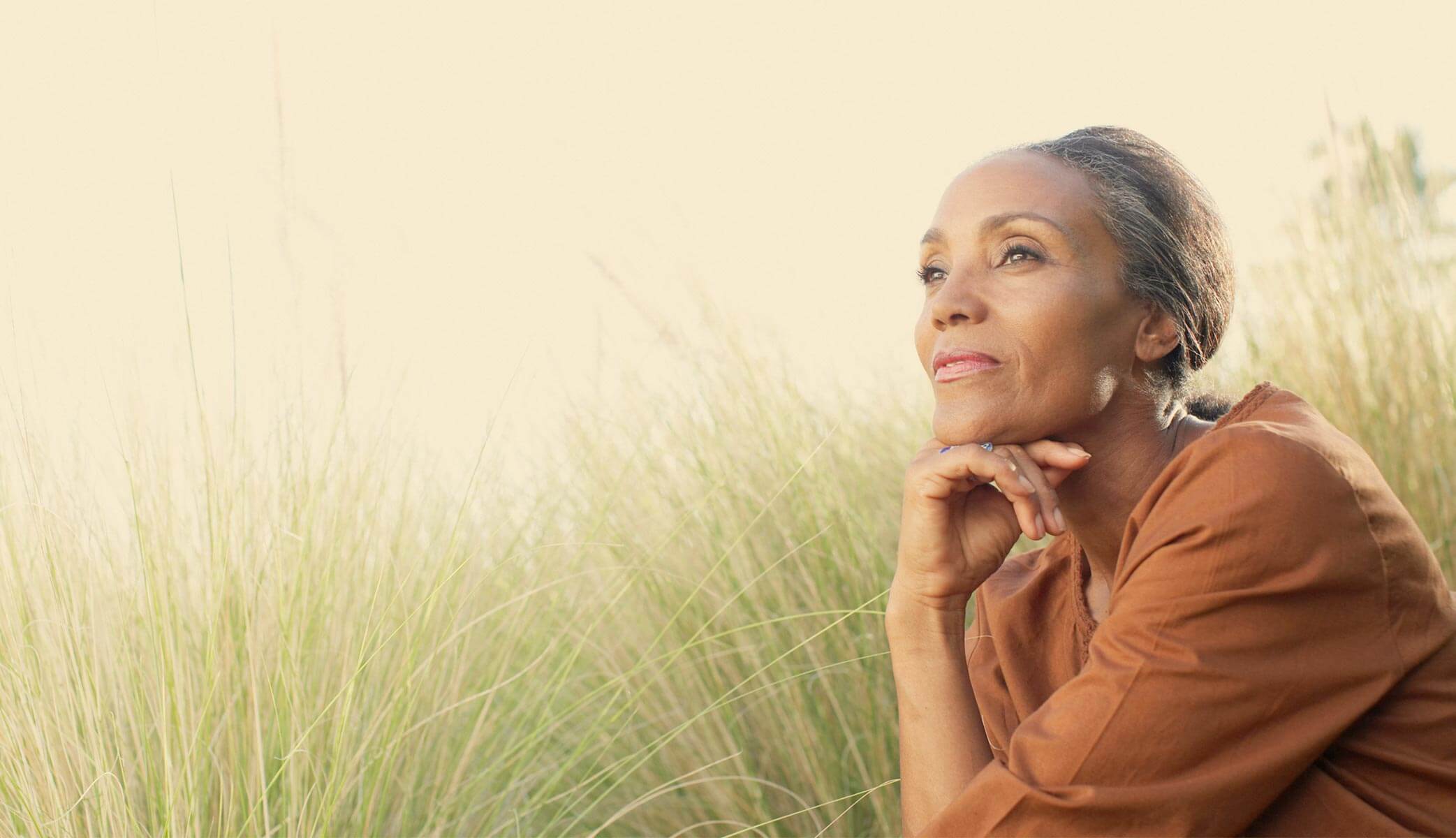 Confident woman thinking dreamily in a grass field